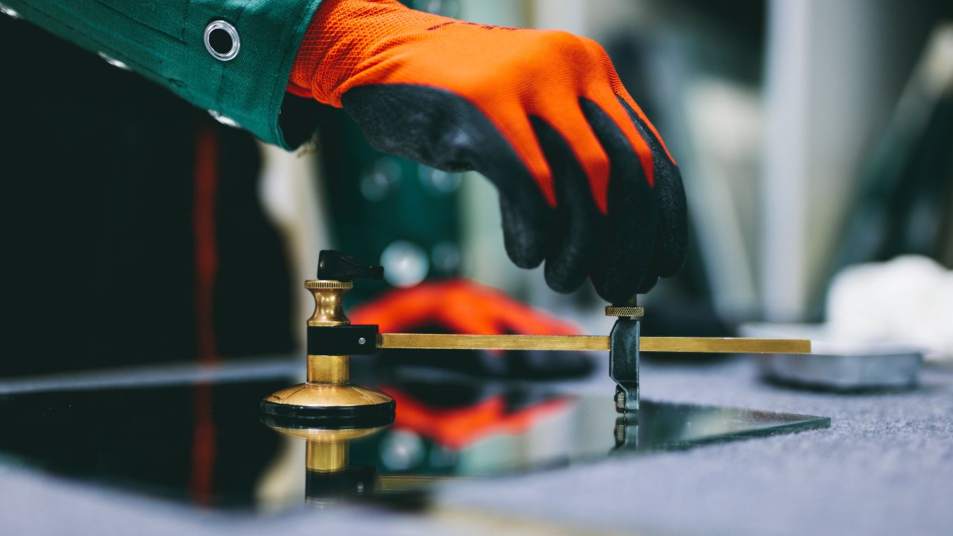 Vitrier utilisant un coupe-verre sur une plaque de verre, portant des gants de protection.